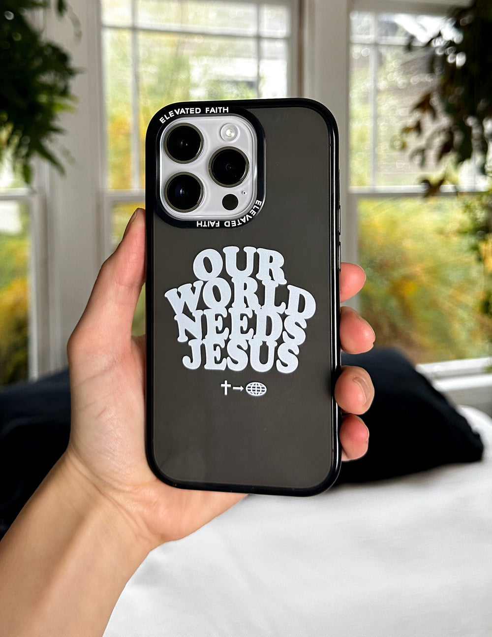 Black phone case held in hand, showing “OUR WORLD NEEDS JESUS” front text
