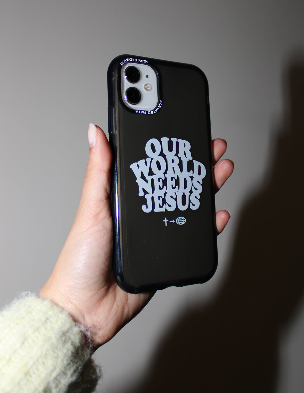 Black phone case held at side, white “OUR WORLD NEEDS JESUS” print