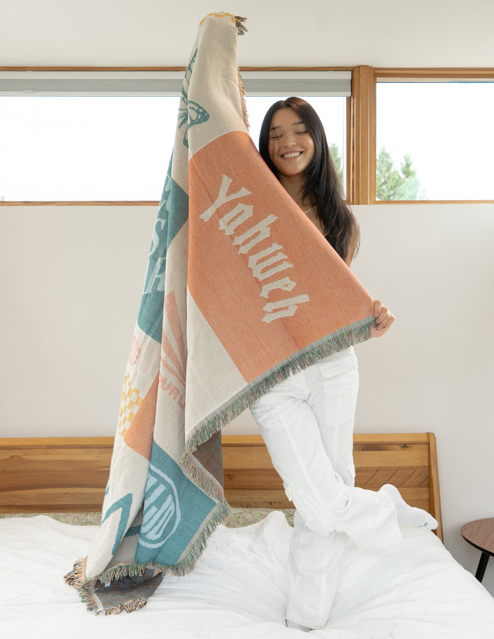 Patchwork throw blanket draped over shoulders, pastel orange and teal typography, fringed