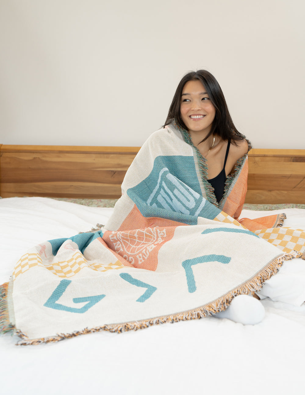 Patchwork throw blanket on bed with teal arrows and coral-orange panels, fringed edge