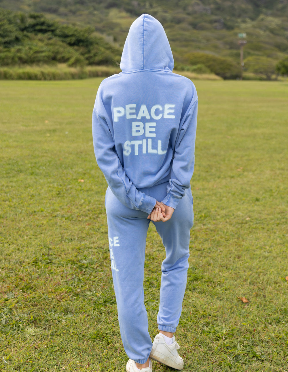 Light blue hoodie with hood up and “PEACE BE STILL” back graphic print