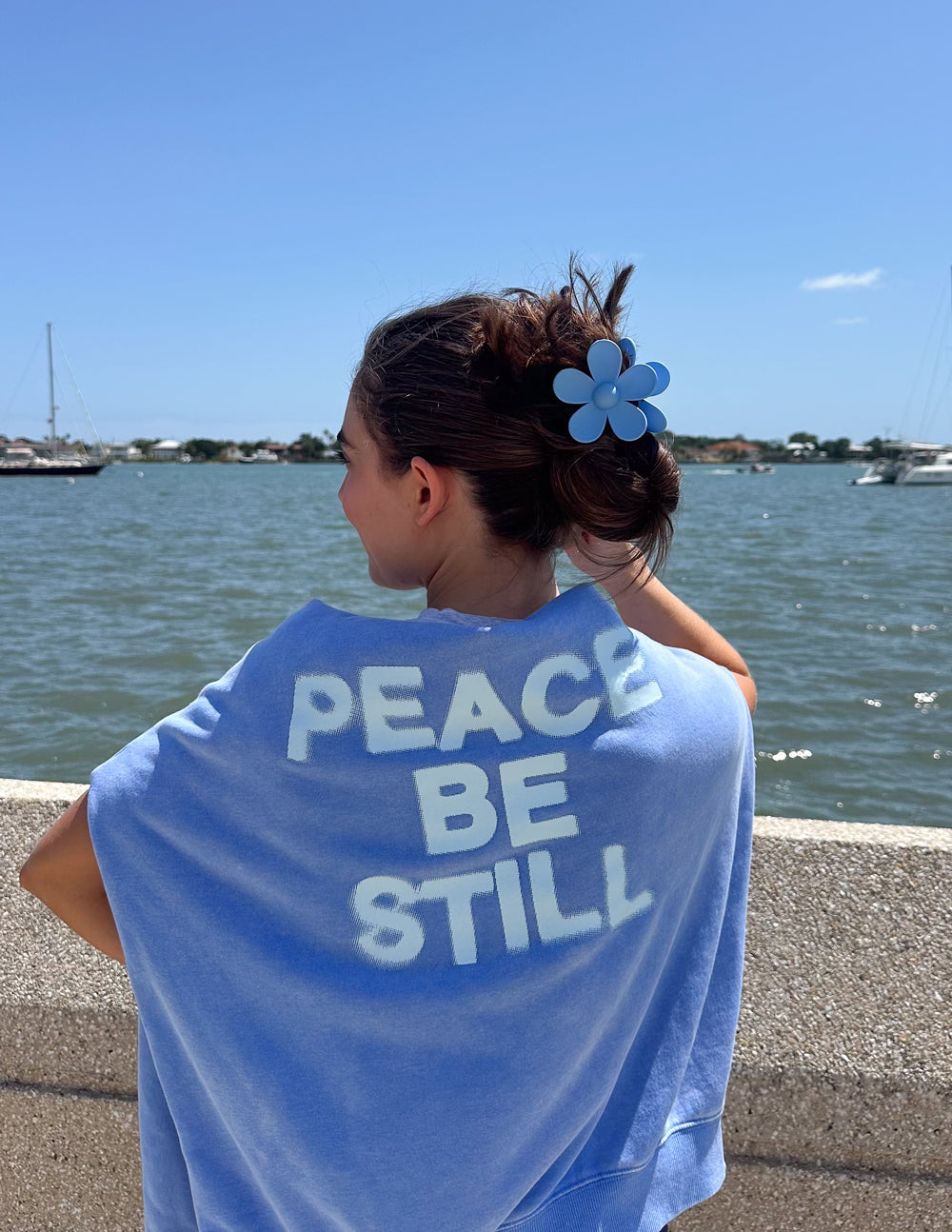Light blue unisex hoodie worn by model, 'PEACE BE STILL' on back