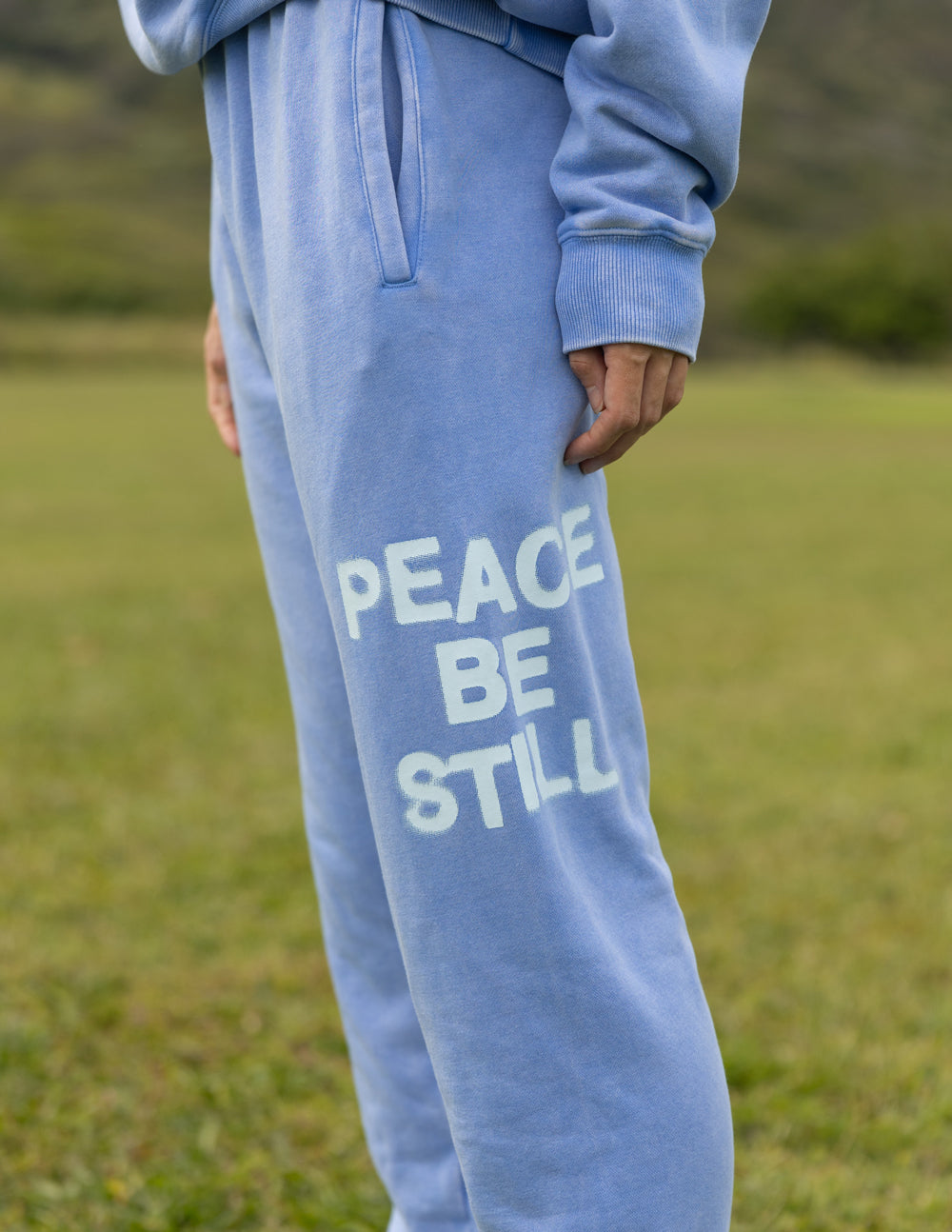 Light blue unisex sweatpants with “PEACE BE STILL” graphic on the thigh