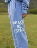 Light blue unisex sweatpants with “PEACE BE STILL” graphic on the thigh