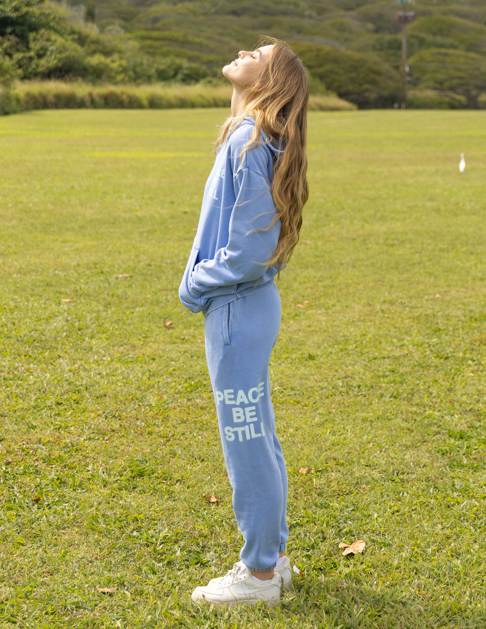Light blue unisex sweatpants with “PEACE BE STILL” text graphic, full-length view