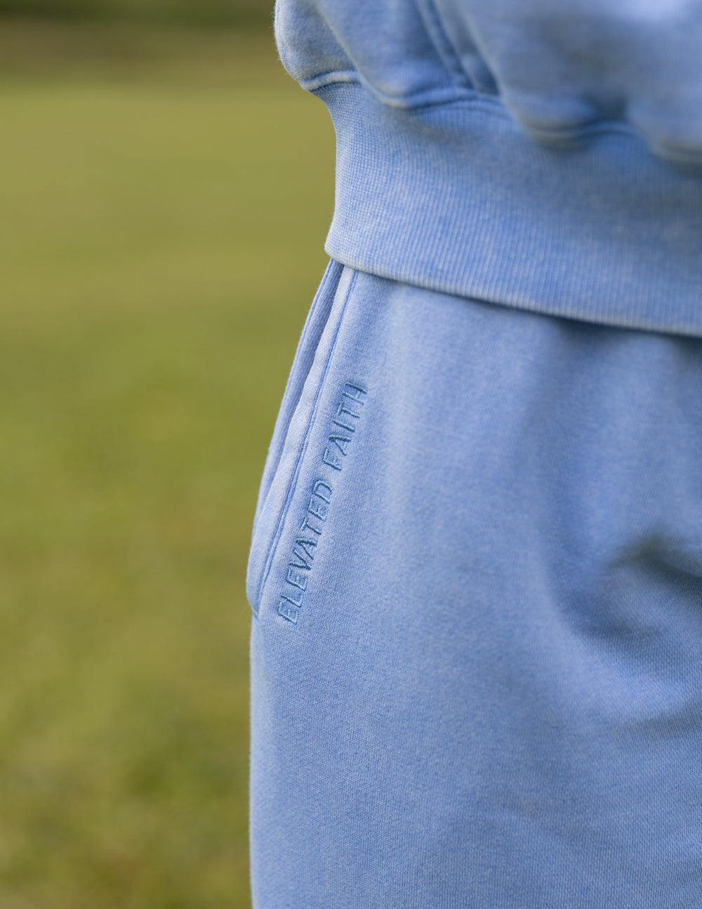 Light blue sweatpants leg with vertical embroidered text near the side seam