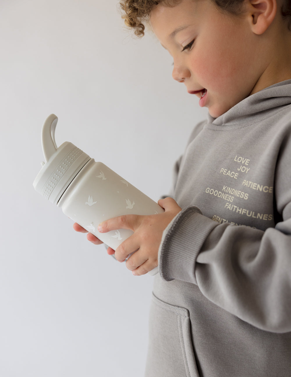 Kids water bottle in pale gray, held by child, flip straw lid