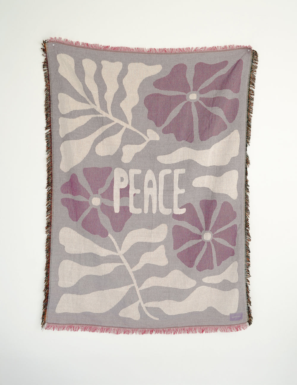 Throw blanket with purple floral pattern, centered 'Peace' print, pink fringed edge