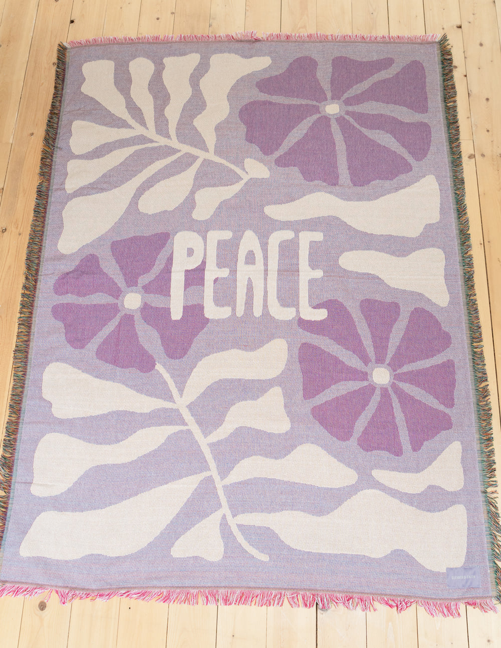 Throw blanket with purple floral design, centered 'PEACE' lettering, pink fringe