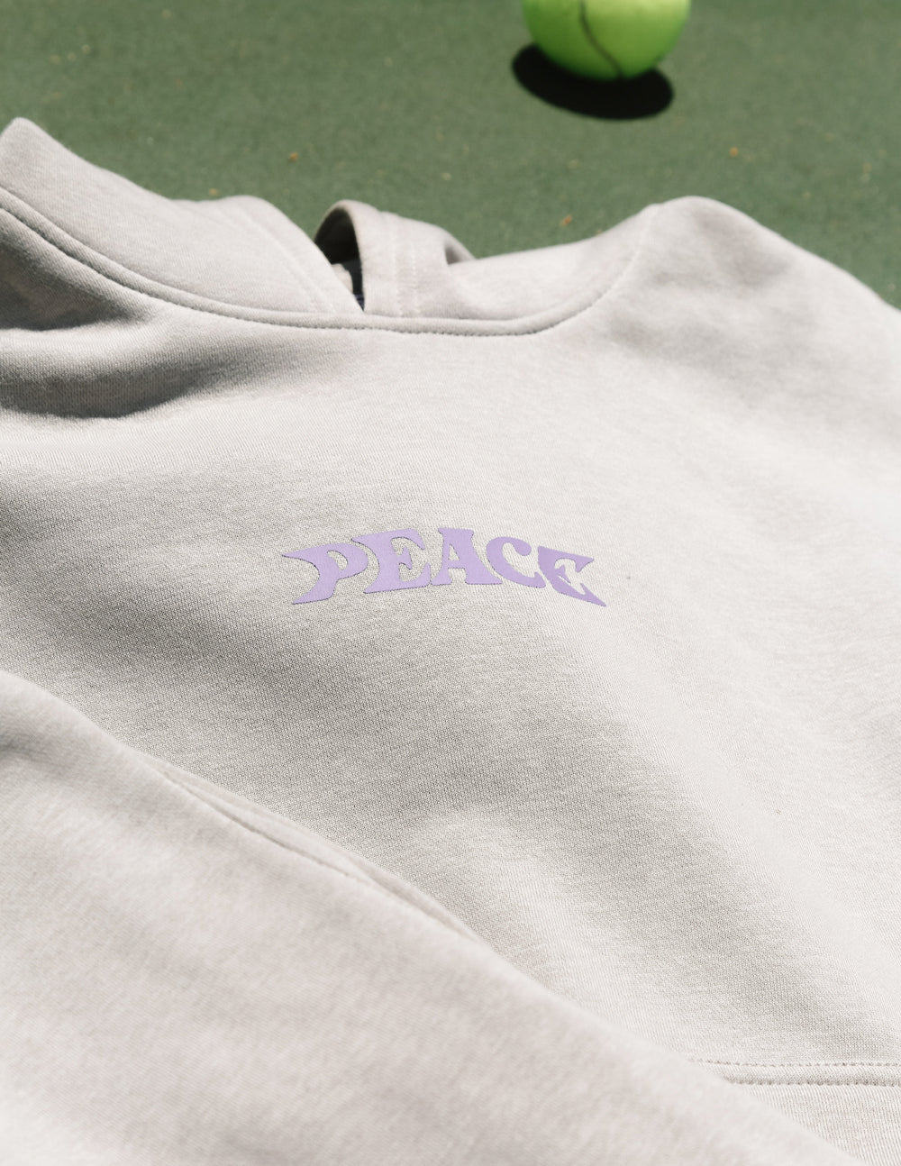 White hoodie close-up with small purple "PEACE" logo on chest