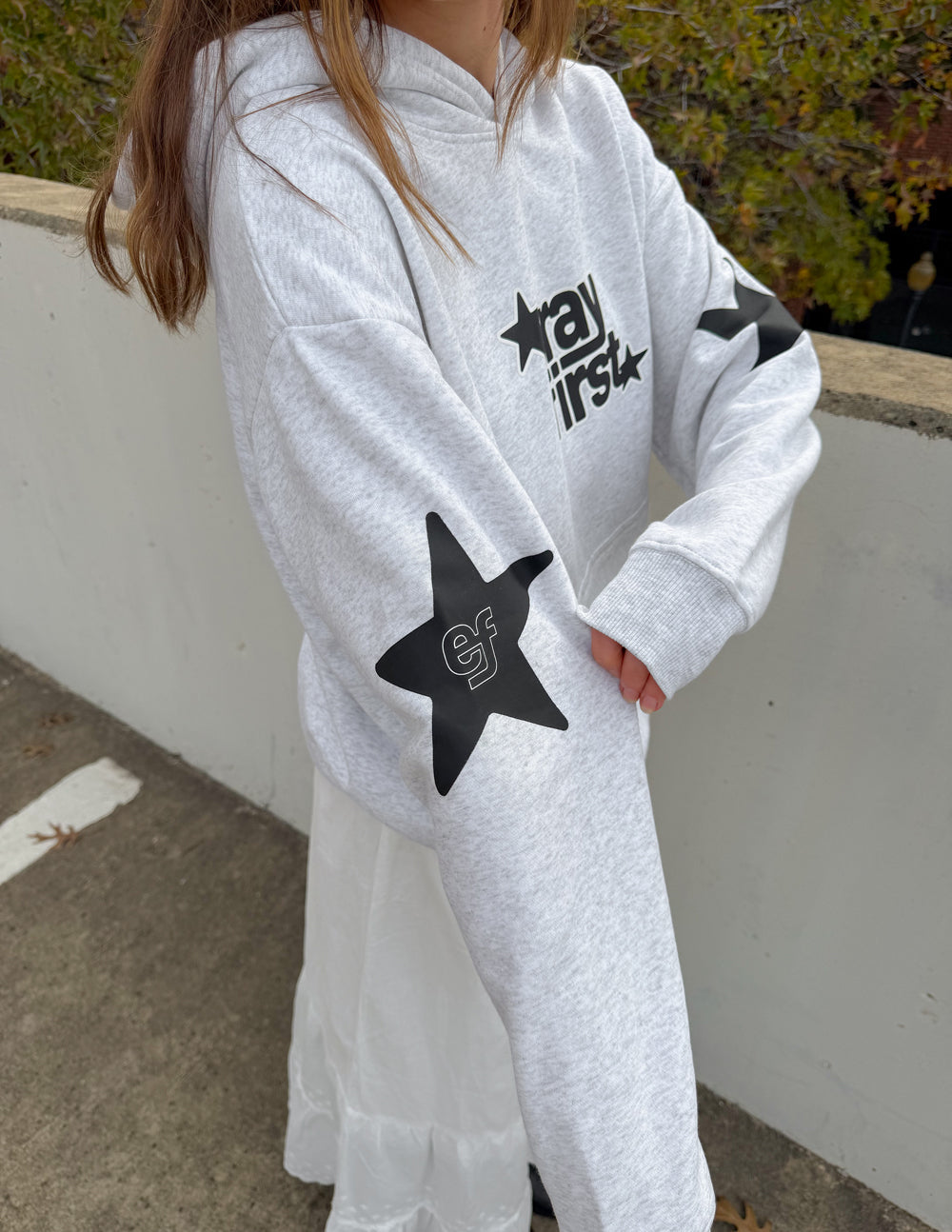 Light gray hoodie with "pray first" chest print, star sleeve graphics, kangaroo pocket