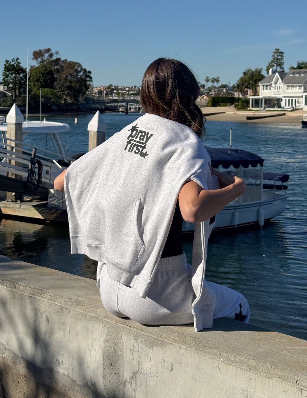 Light gray unisex hoodie, back view showing "pray first" text logo and hood