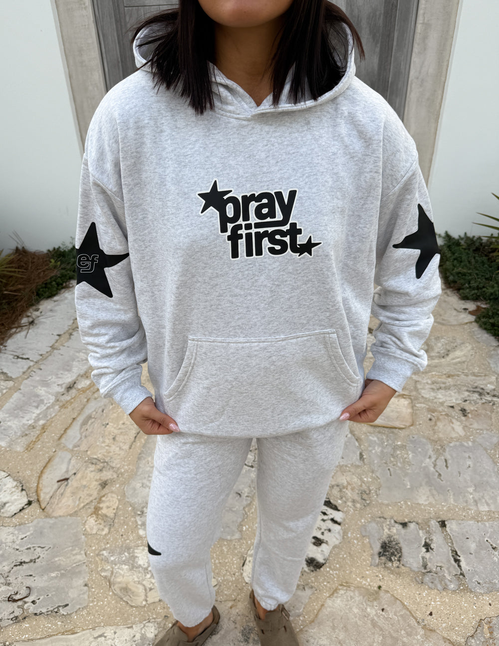 Light gray hoodie with "pray first" chest graphic and star sleeve details, kangaroo pocket