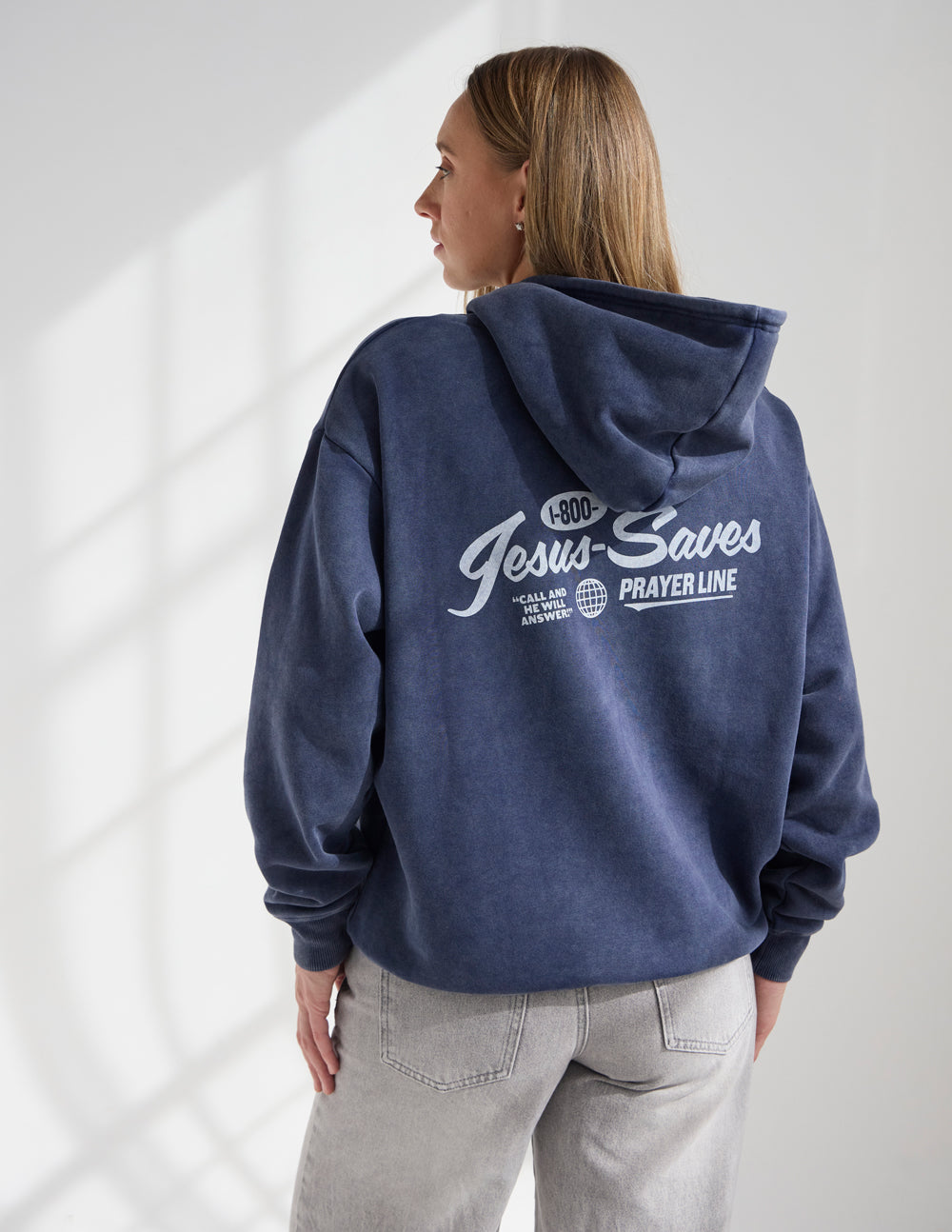 Dark navy unisex hoodie worn from back, hood and “Jesus Saves Prayer Line” print