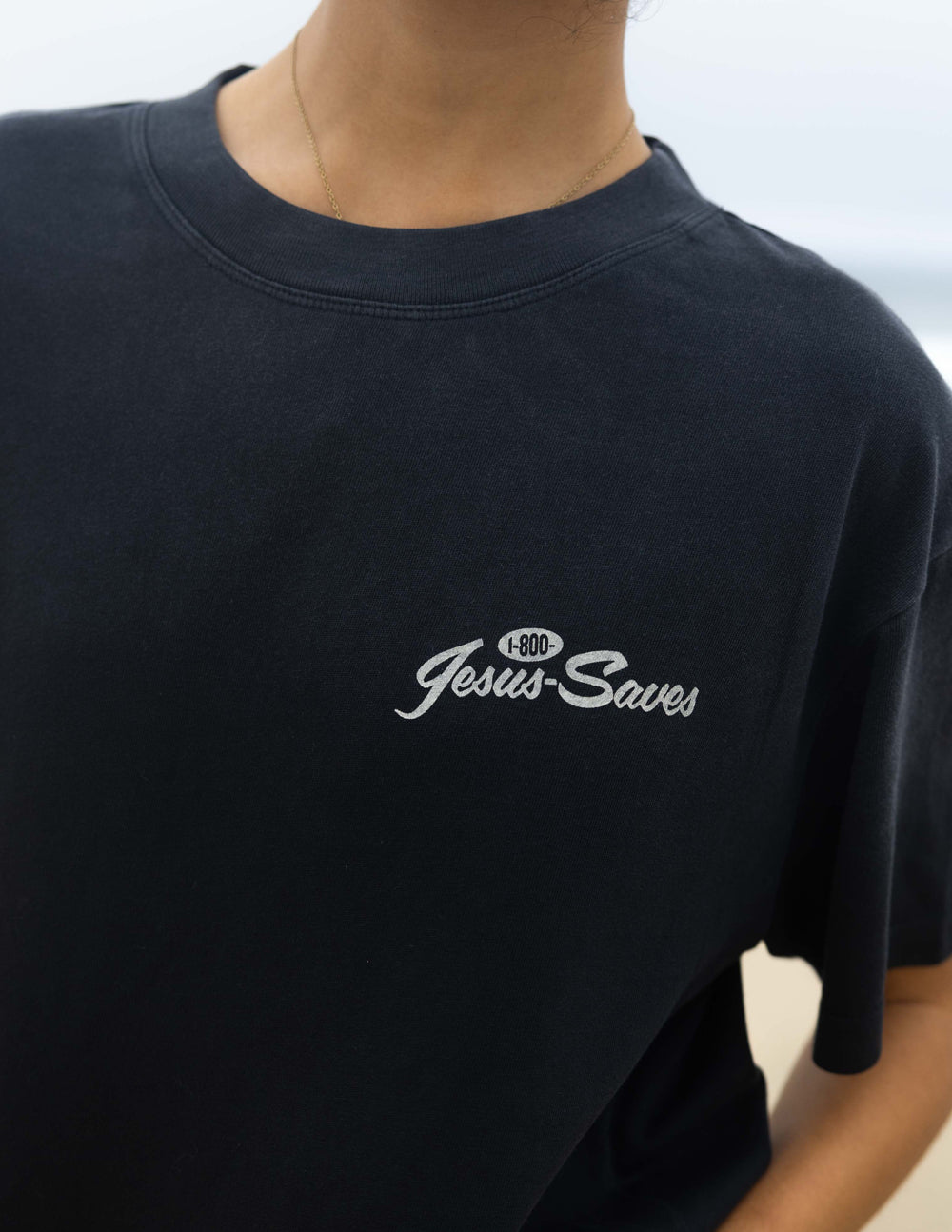 Black unisex T-shirt chest close-up of 'Jesus Saves' script logo
