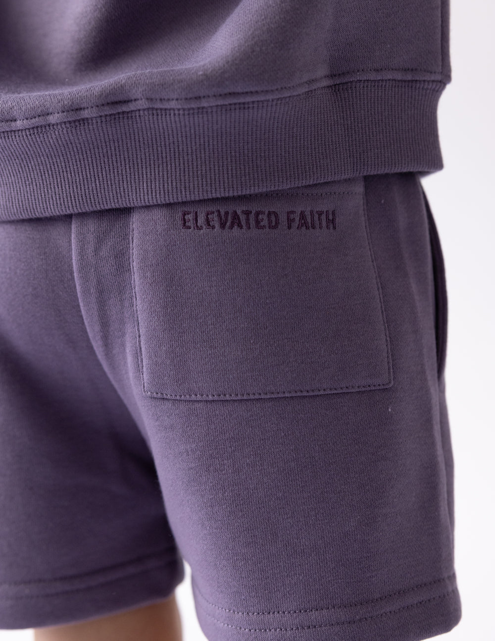 Kids purple short with “ELEVATED FAITH” text on front pocket