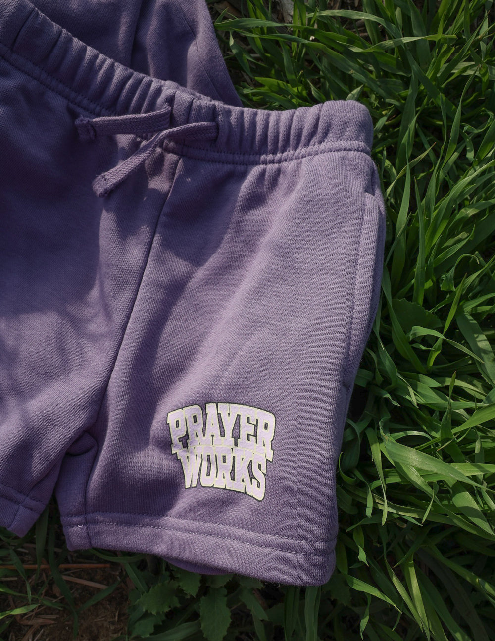 Kids purple drawstring short with PRAYER WORKS logo near hem