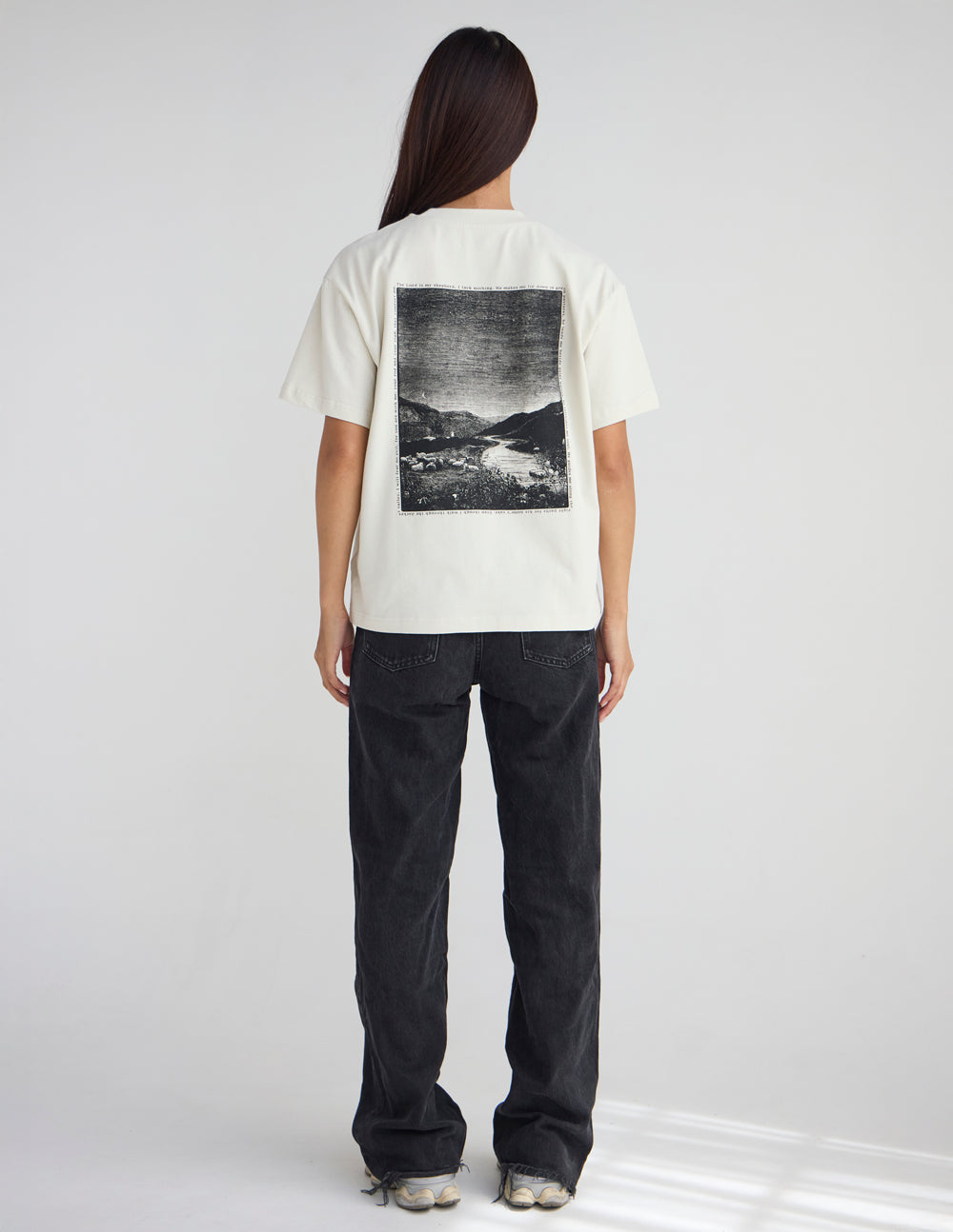 Cream unisex T-shirt with square landscape graphic on back; dark jeans