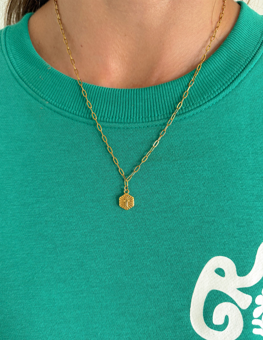 Gold-tone chain necklace with a small radiant pendant shown at neckline