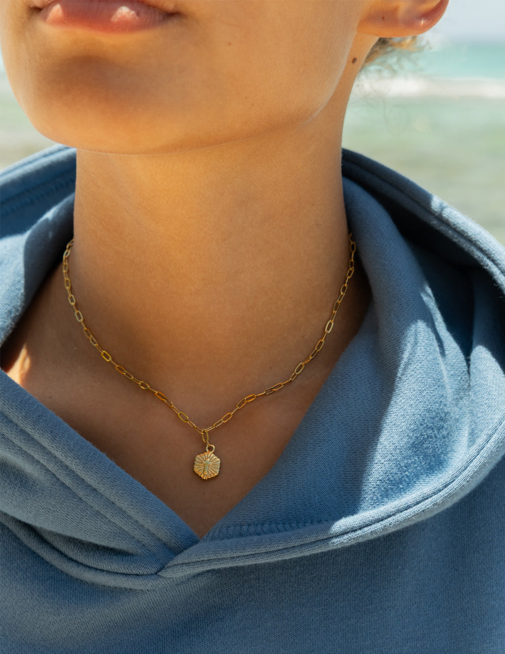 Gold-tone chain necklace with radiant pendant resting at the collarbone