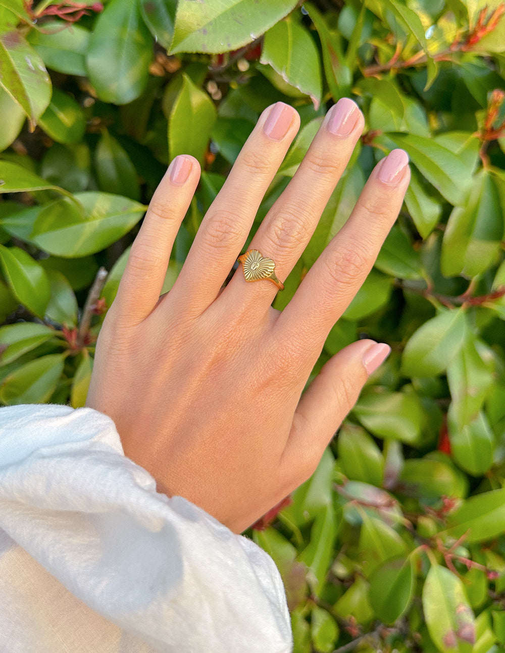 Gold heart ring with cross center and radiant rays on finger