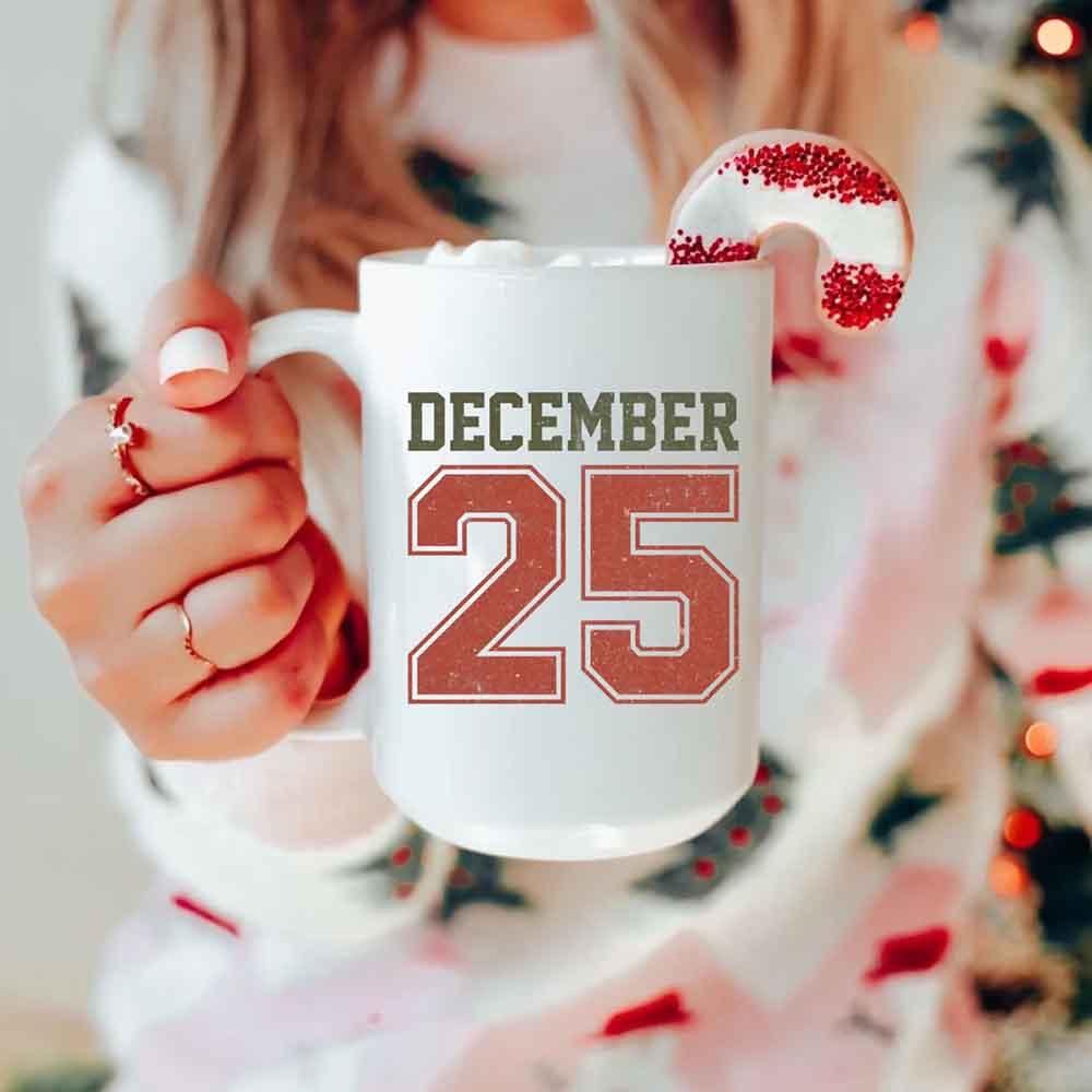 White mug with 'DECEMBER 25' graphic, shown being held.