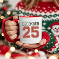 White coffee mug with red rim and handle, 'DECEMBER 25' print.
