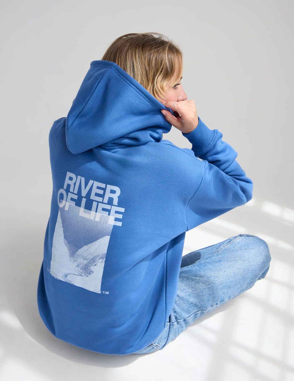 Blue hoodie back view with large “RIVER OF LIFE” print and hood.