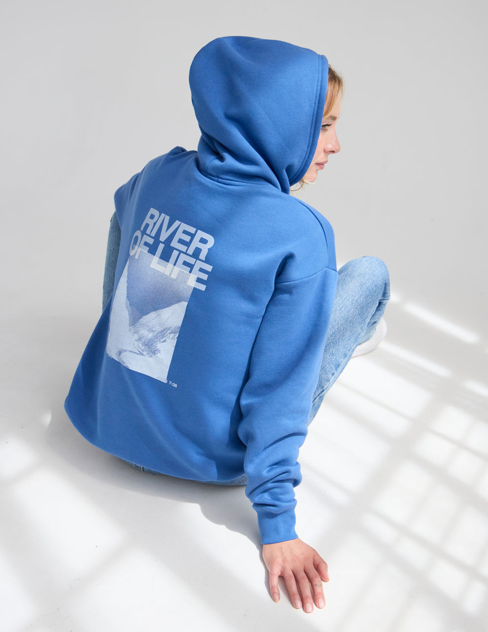 Blue hoodie with hood up and large “RIVER OF LIFE” back print.
