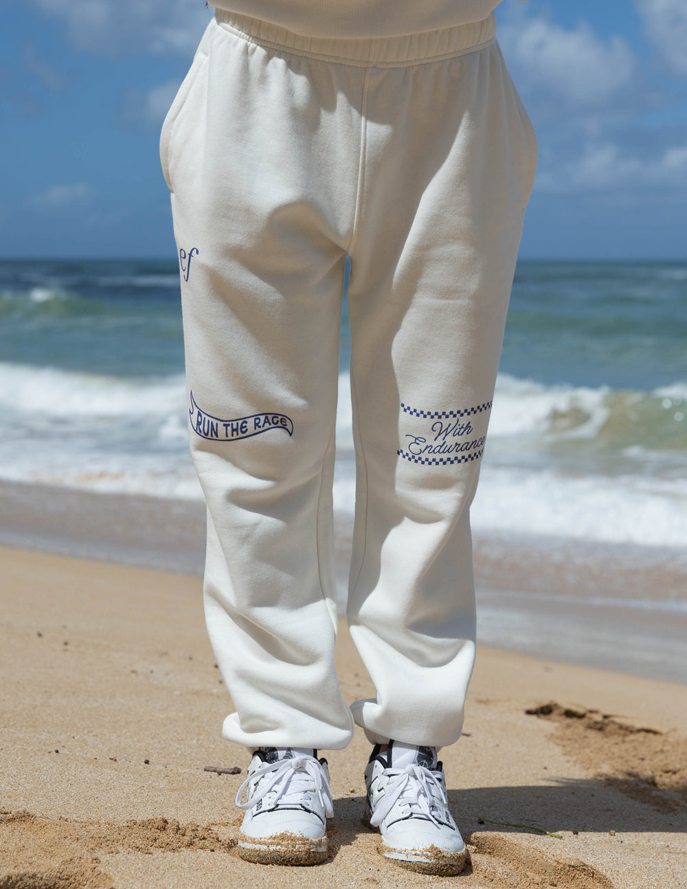 White sweatpants with front seams, side pockets, and blue logo patches