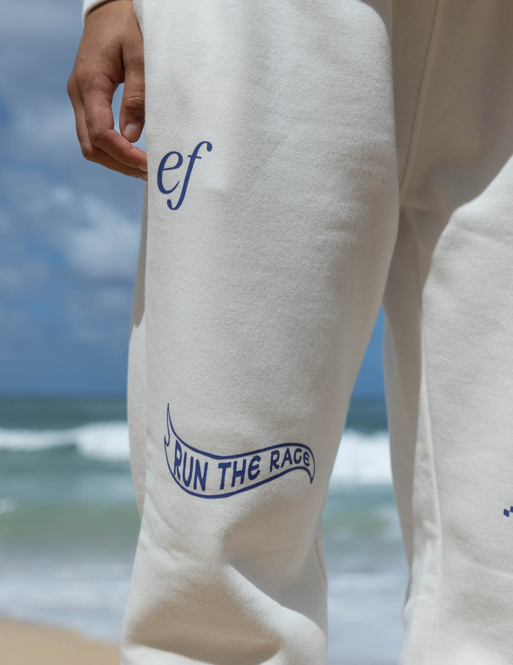 White sweatpants with blue “Run the Race” logo on the lower left leg