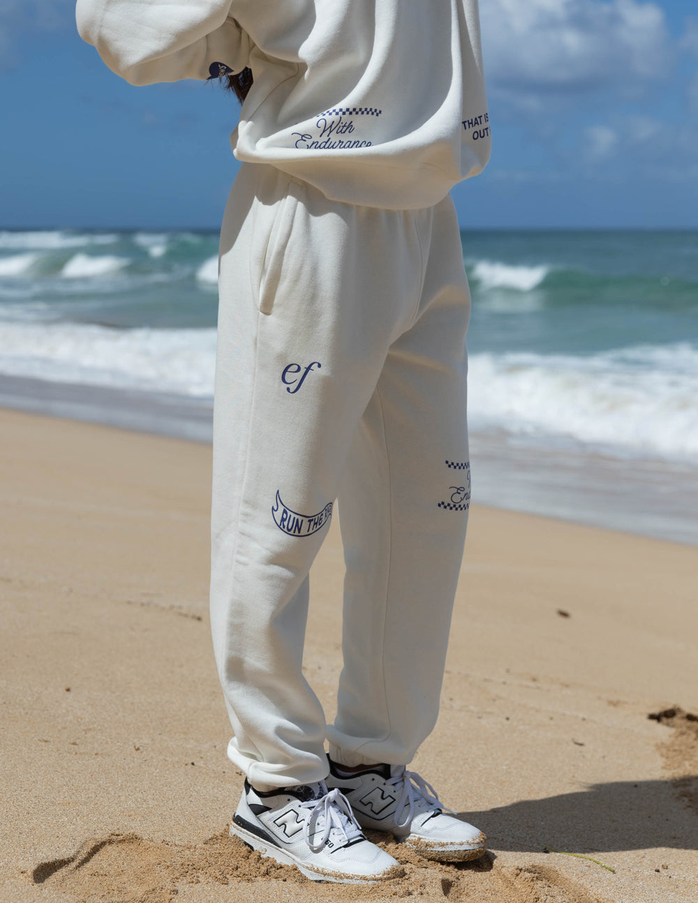 White sweatpants with blue logo embroidery on leg and elastic cuff hems