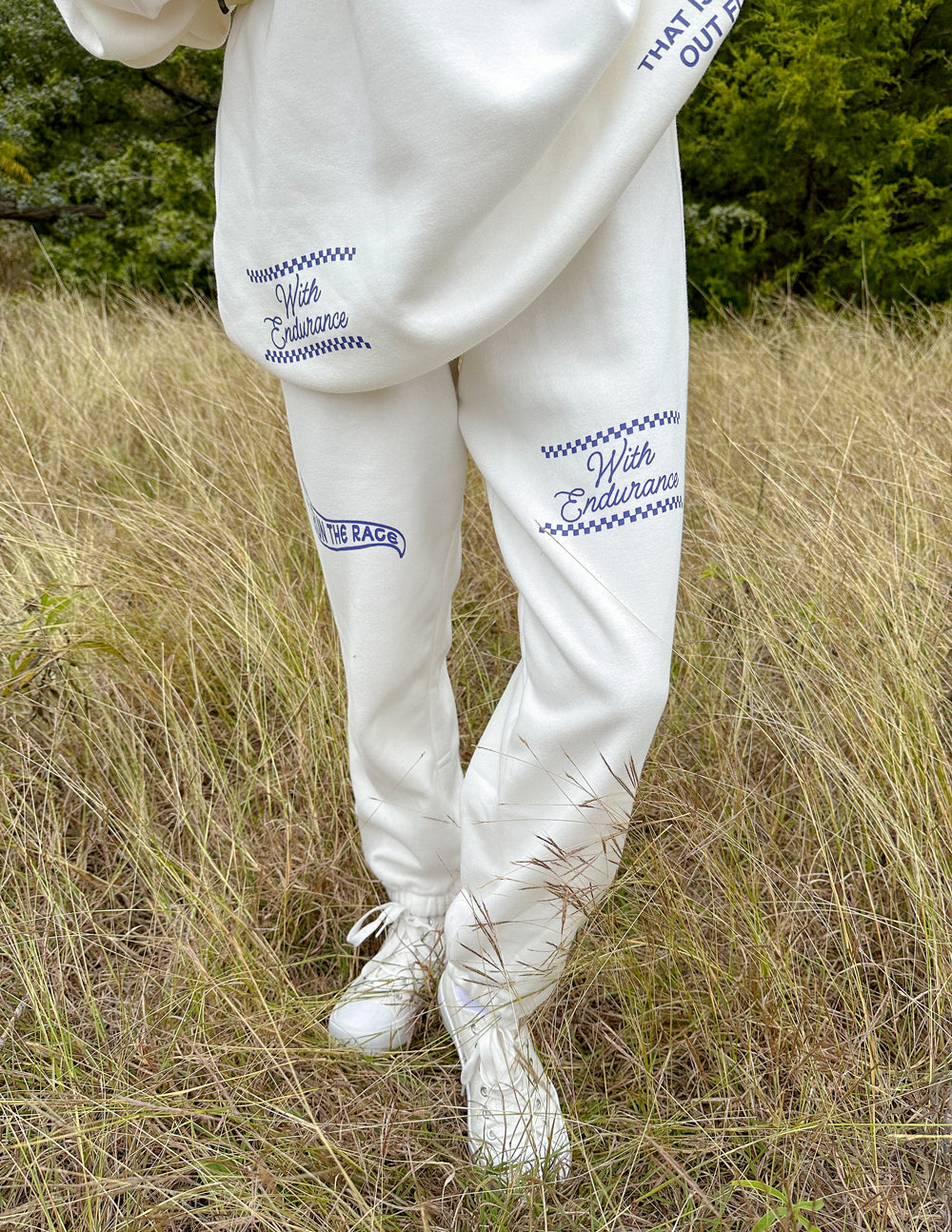White sweatpants with blue logo embroidery on left thigh and right ankle cuff