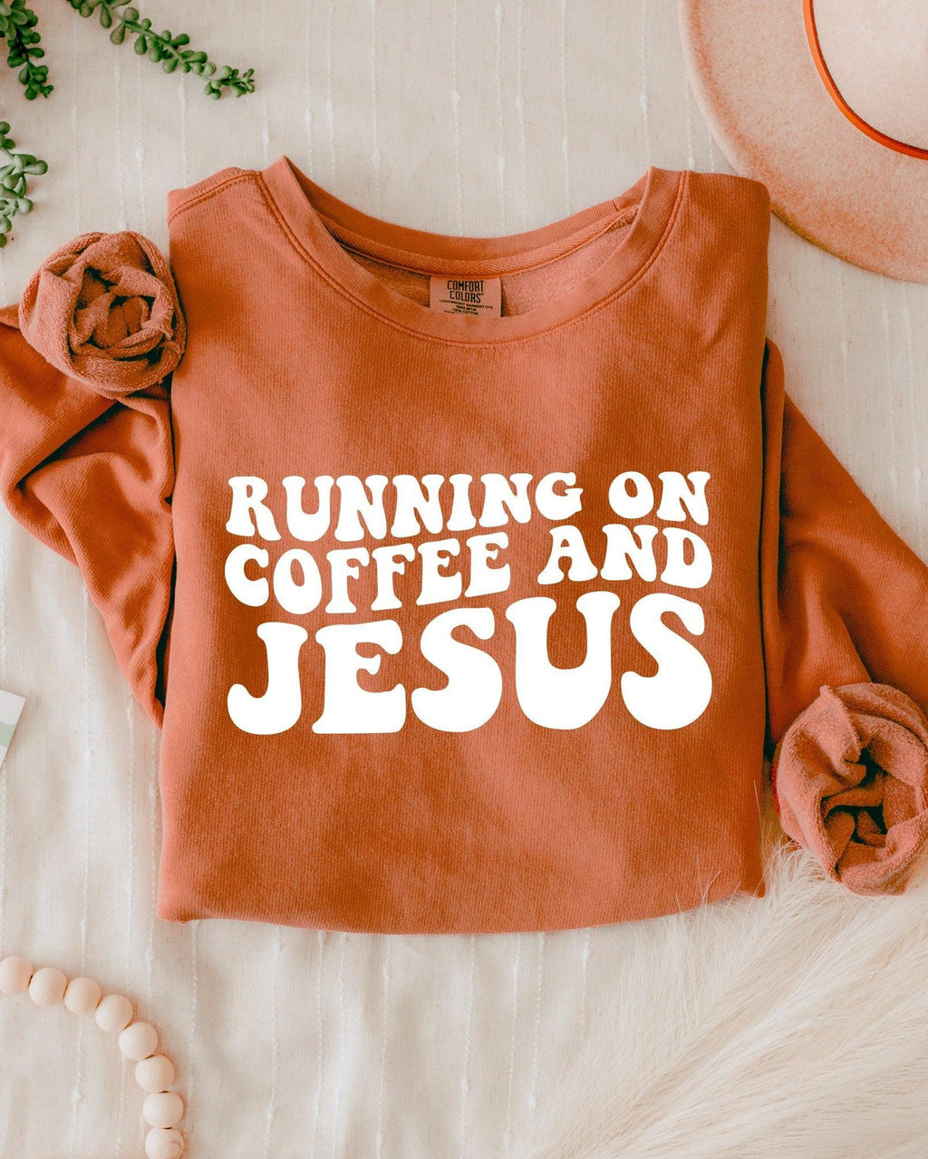 Rust orange sweatshirt with bold "RUNNING ON COFFEE AND JESUS" text front.