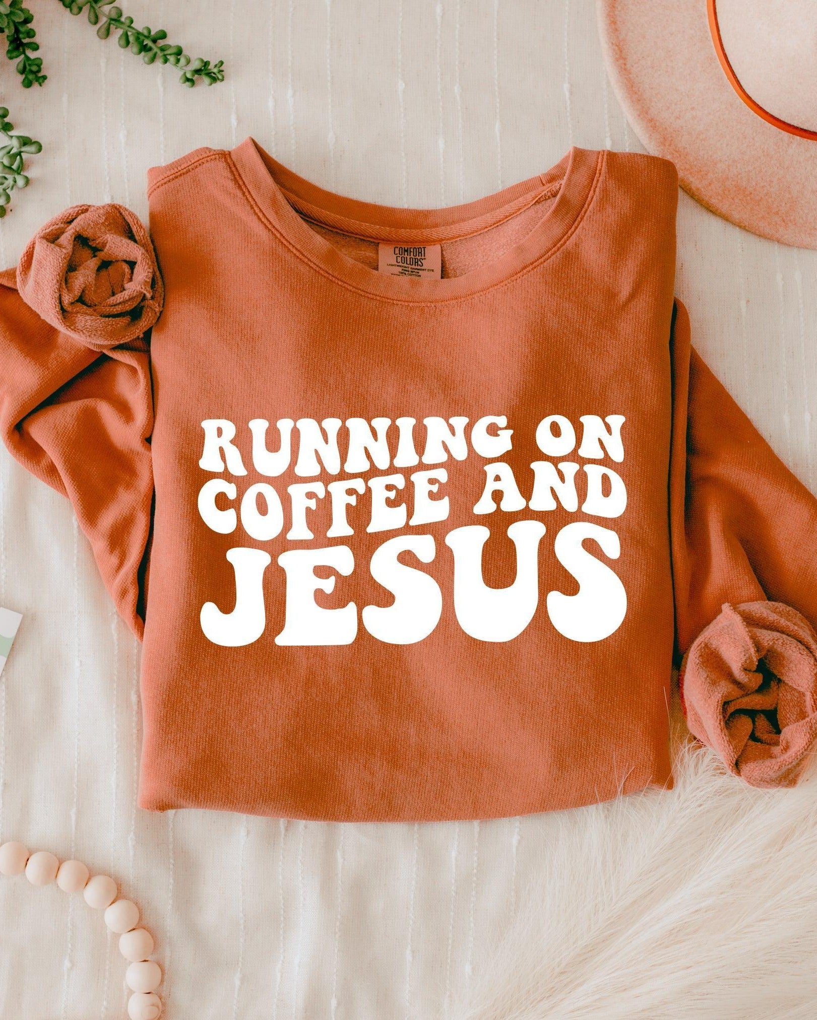 Rust orange sweatshirt with bold "RUNNING ON COFFEE AND JESUS" text front.