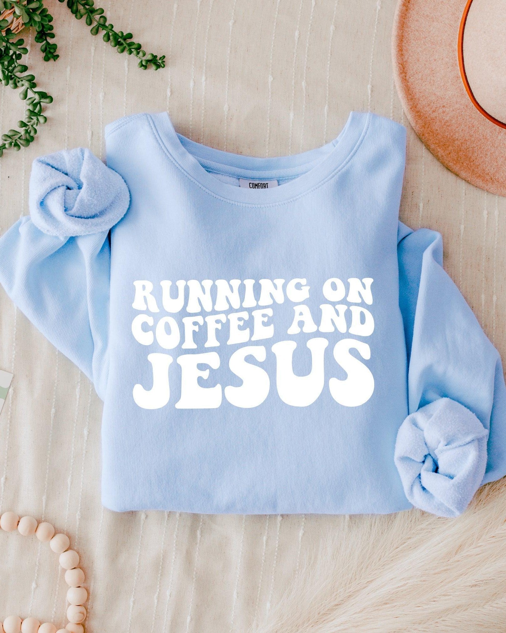 Light blue sweatshirt with bold "RUNNING ON COFFEE AND JESUS" text front.
