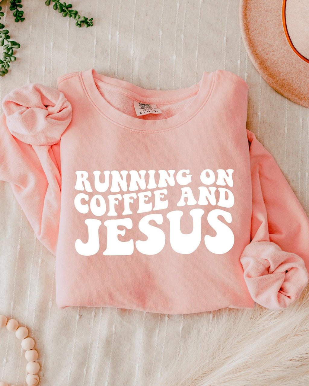 Light pink sweatshirt with bold "RUNNING ON COFFEE AND JESUS" text front.