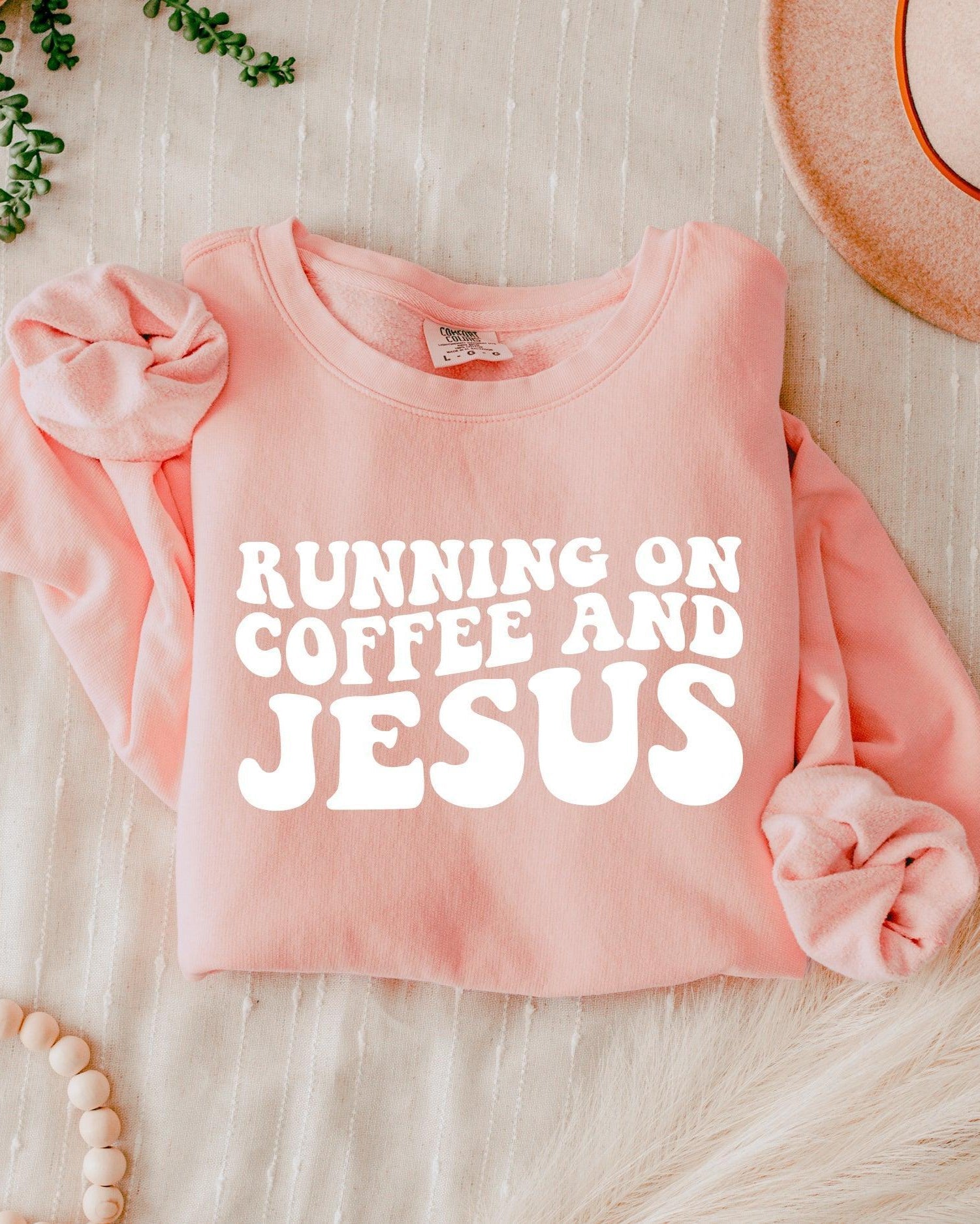 Light pink sweatshirt with bold "RUNNING ON COFFEE AND JESUS" text front.
