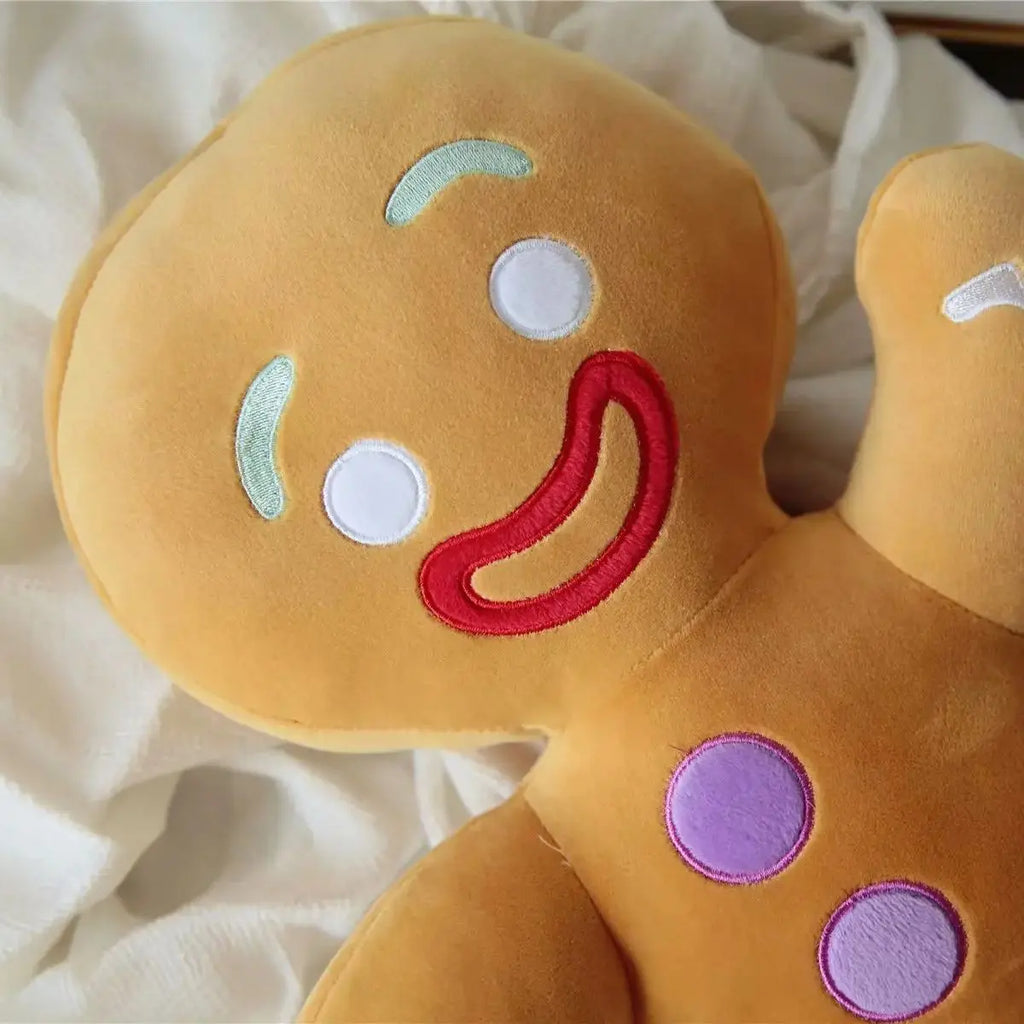 Close-up gingerbread man plush head and arm with red smile, white icing outlines, purple button.