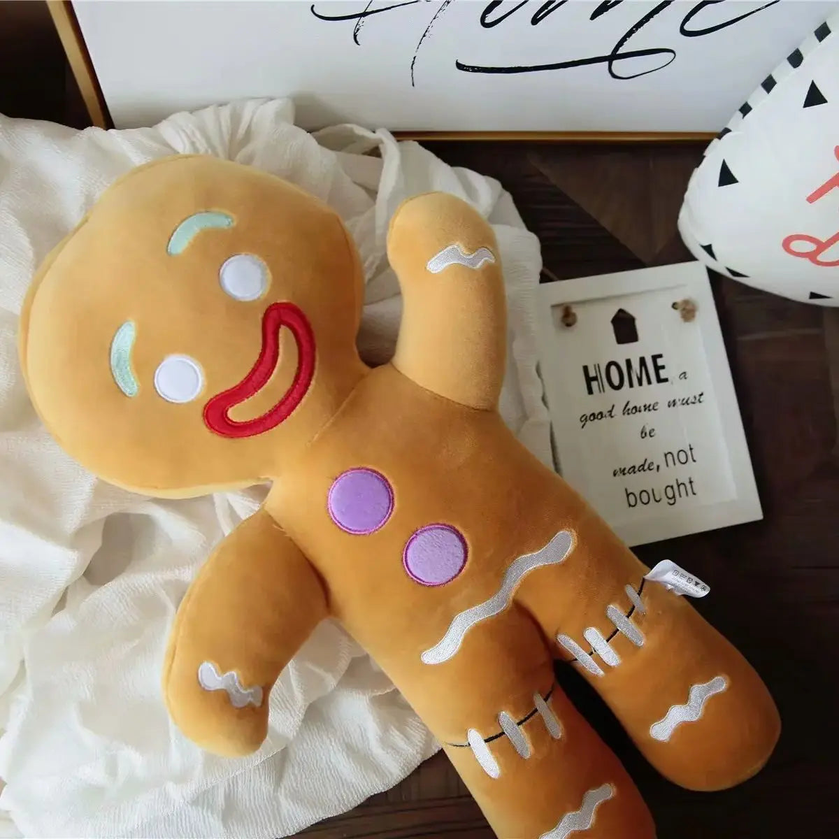 Tan gingerbread man plush with red smile, blue eyes, purple buttons and white icing details.