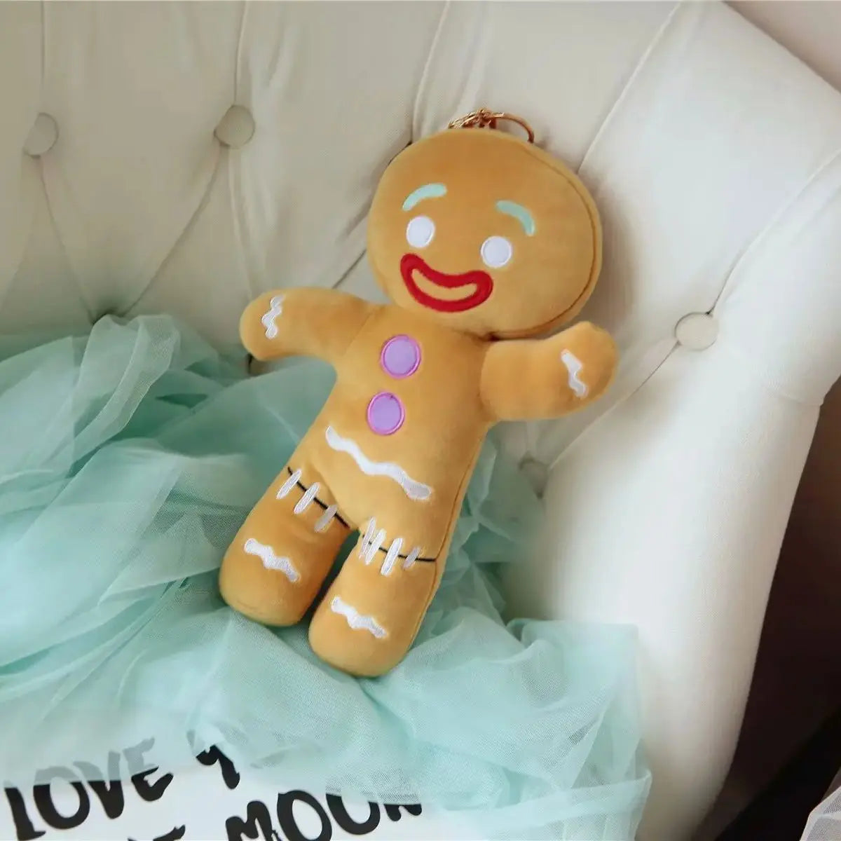 Gingerbread man plush sitting on bed with red smile, purple buttons, and stitched white icing shoes.