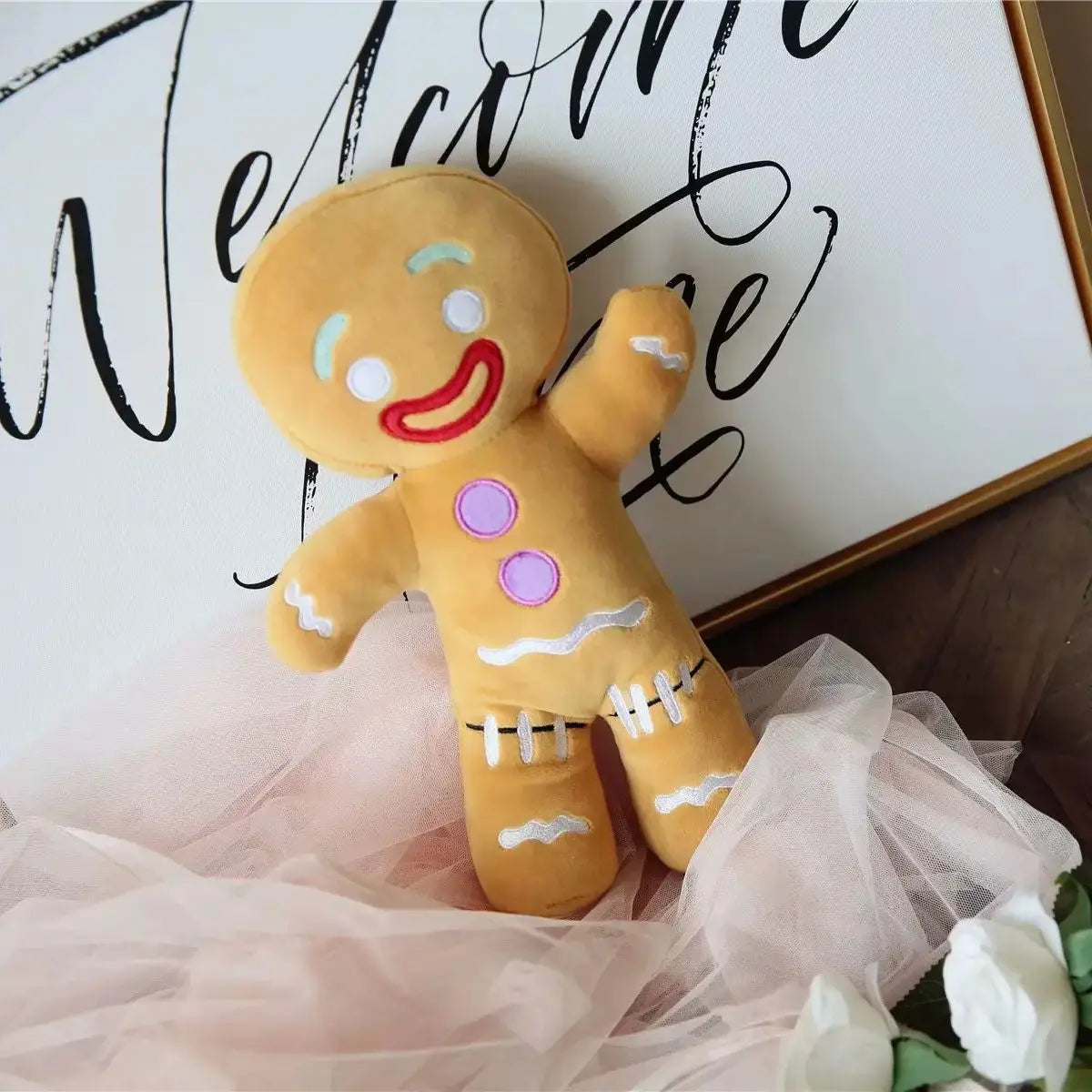 Gingerbread man plush in tulle skirt with red smile, purple buttons, and white icing lacing on feet.