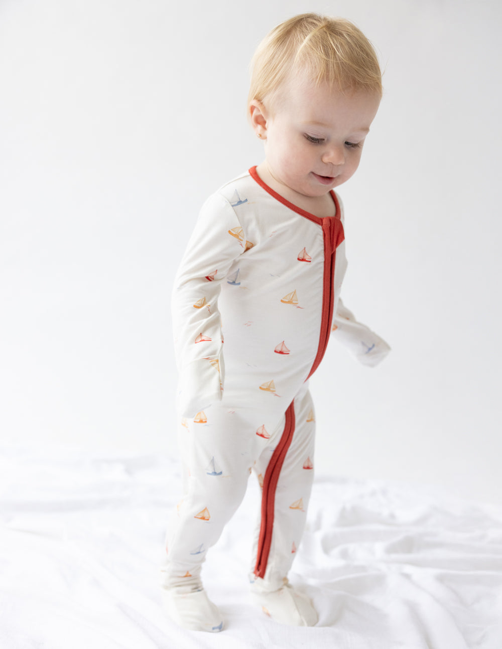 Footed onesie with sailboat print, red zip-front, long sleeves on toddler standing