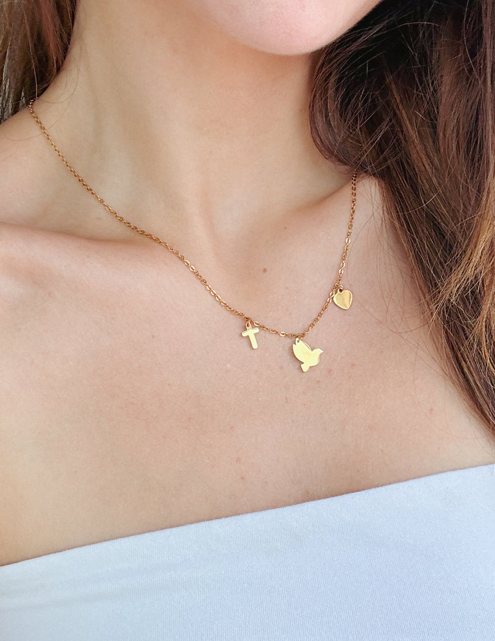 Gold-tone charm necklace with cross, heart, and butterfly charms on a fine chain