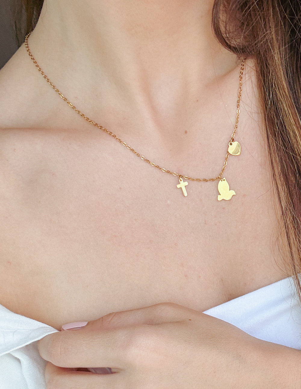 Gold-tone charm necklace with small heart, cross, and butterfly charms near neckline