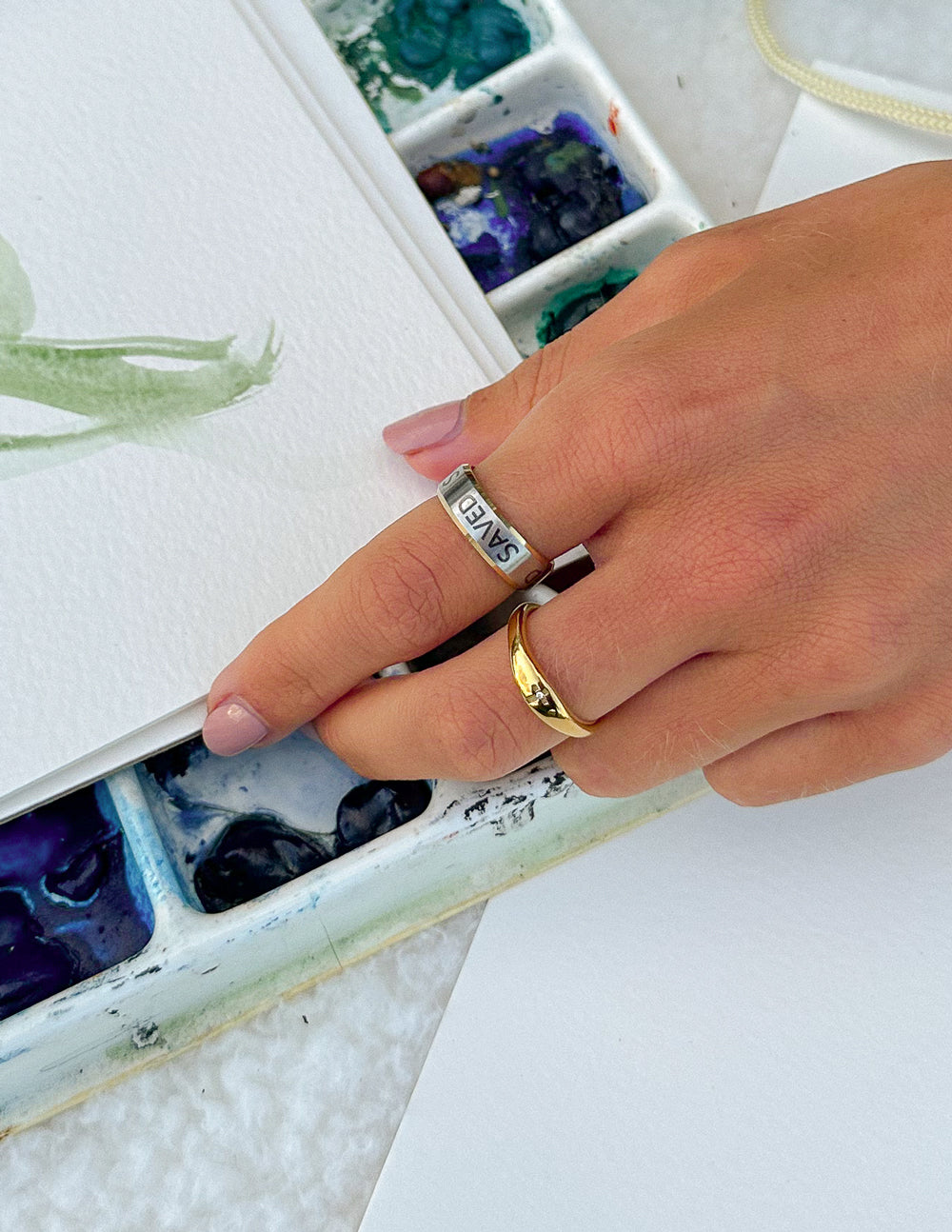 Gold ring with 'SAVED' engraving on finger, angled view