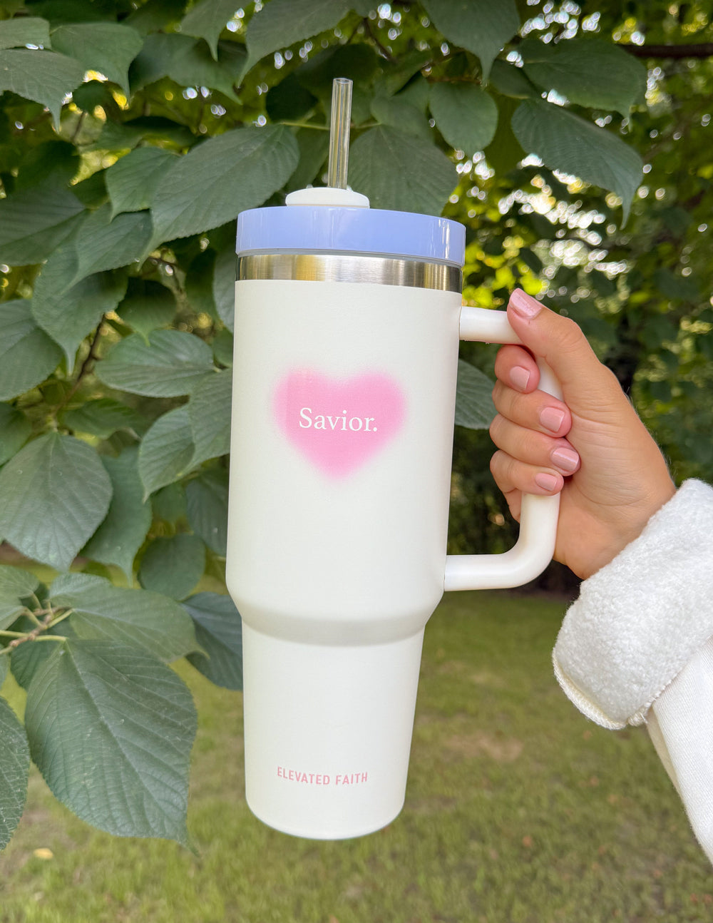 White 40 oz tumbler with pink heart logo, silver lid and straw, held at the handle