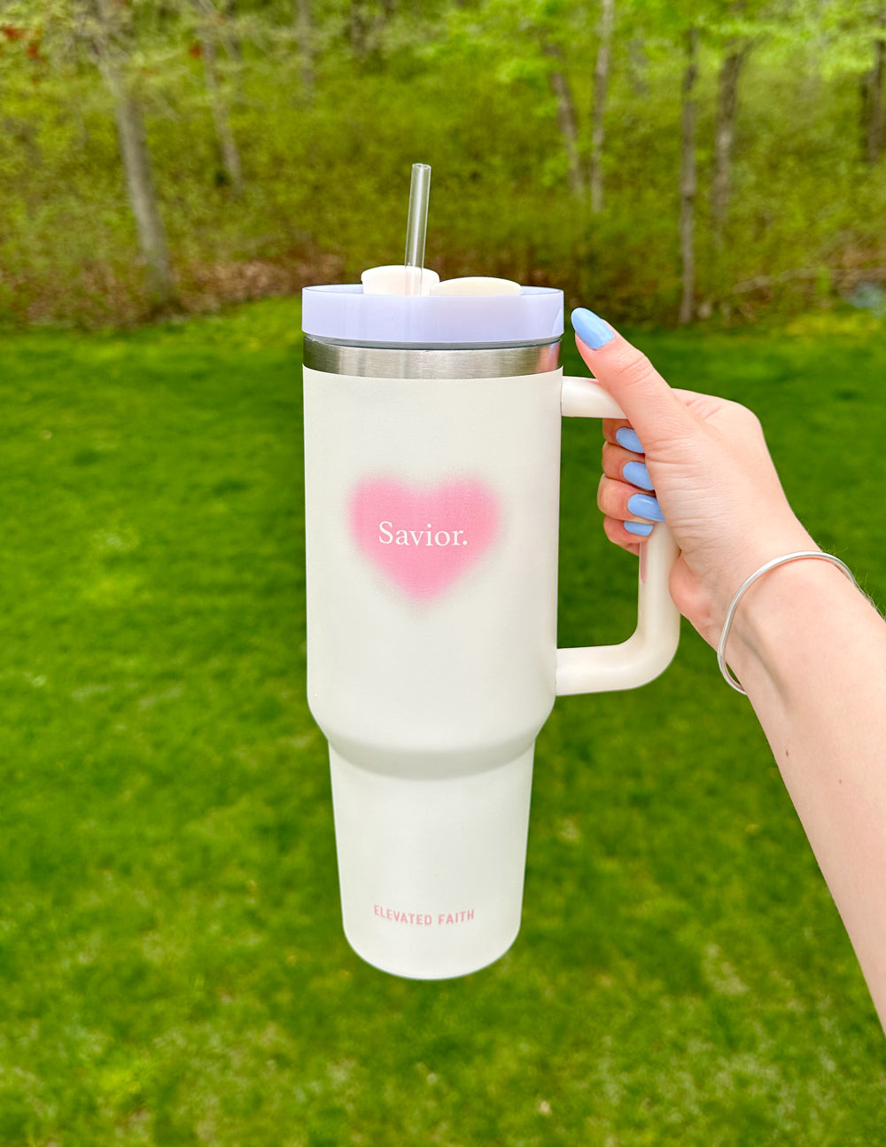 White 40 oz tumbler with pink heart logo, silver lid and straw, grasped by handle