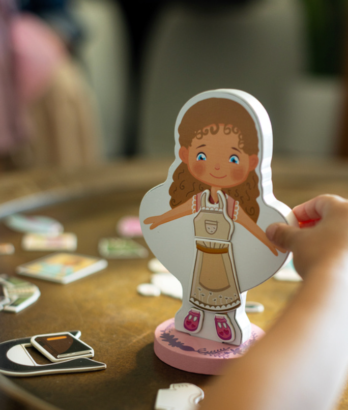 Magnetic wooden dress-up doll of a girl on a pink base, held by a hand