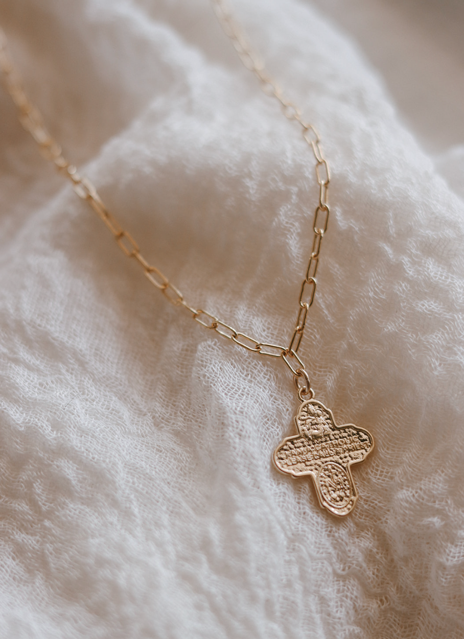 Gold paperclip chain necklace with textured cross pendant on fabric
